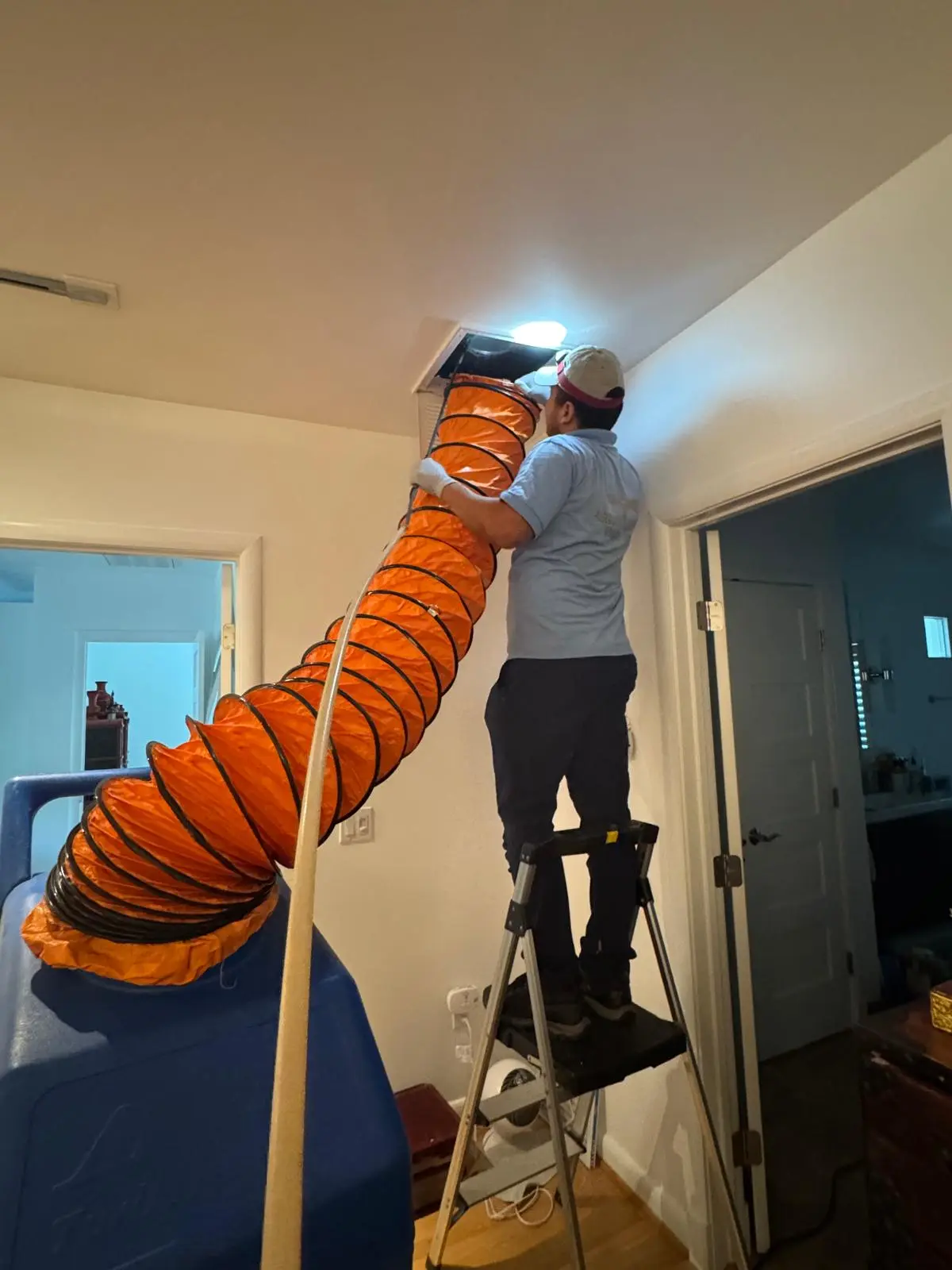CleanFlow Pros technician on a ladder running a collection hose into a ceiling air duct register